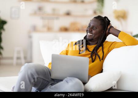 Portrait Of Smiling Black Man With Laptop Relaxing In Chair At Home Stock Photo