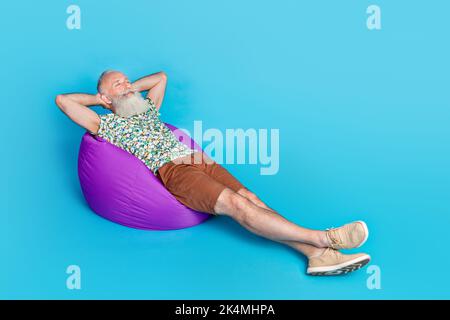 Full size photo of peaceful positive person sit laying comfy bag take nap isolated on blue color background Stock Photo
