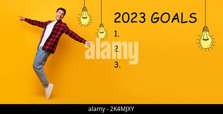 Happy millennial caucasian guy dancing, look at 2023 goals inscription with light bulbs, checklist Stock Photo