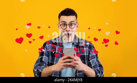 Shocked handsome young guy in glasses looking at his smartphone Stock Photo