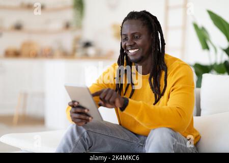 Technologies For Leisure. Black Happy Man Using Digital Tablet At Home Stock Photo