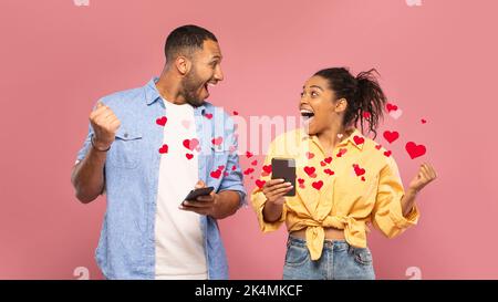 Excited young black couple using mobile phones and gesturing Stock Photo
