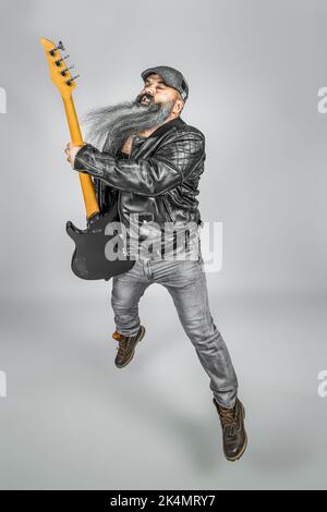 rocker with guitar and long beard performing a jump while playing Stock Photo