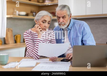 Upset Elderly Couple Checking Financial Documents While Calculating Family Budget At Home Stock Photo