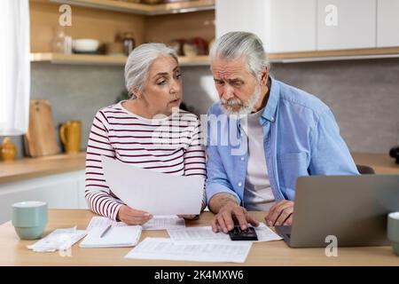 Elderly Spouses Calculating Family Expenses While Sitting On Table In Kitchen Stock Photo