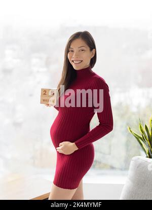 Asian pregnant woman showing 25 weeks pregnancy bump for maternity photoshoot holding wooden blocks sign happy. Vertical crop Stock Photo