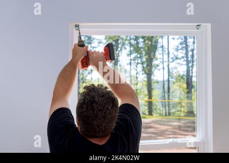 This is a professional technician installing blinds on the windows of a newly constructed home by screwing the fasteners in Stock Photo