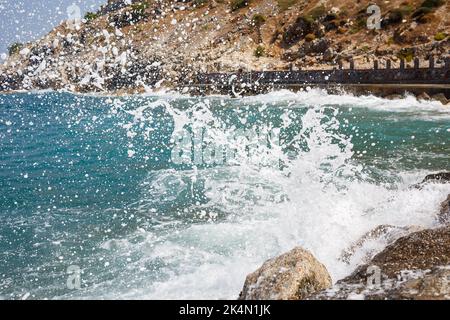 Sea water beats against rocky rocks and makes waves with foam, rugged pier in the sea Stock Photo