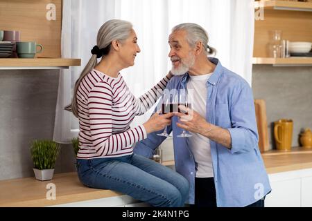 Domestic Date. Loving Senior Spouses Drinking Wine And Chatting In Kitchen Interior Stock Photo