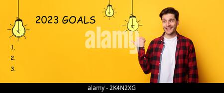 Cheerful millennial european guy point finger at goals 2023 with light bulbs, checklist with blank space Stock Photo