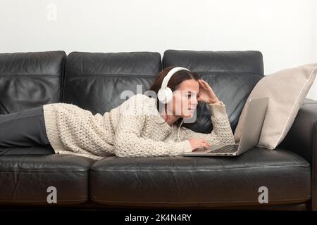 Woman laying on a sofa wearing heaphones with a laptop computer. Stock Photo