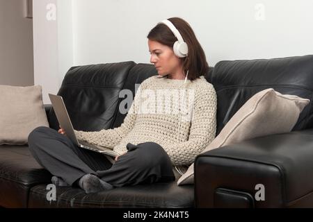 Woman sitting on a sofa wearing headphones with a laptop computer Stock Photo