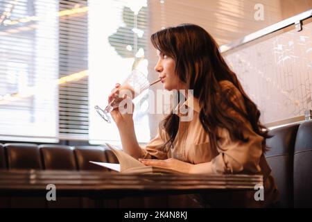 Young thoughtful woman drinking chocolate milkshake in cafe Stock Photo