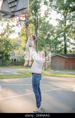Caucasian father holds 2 year old son up to basketball hoop. Stock Photo