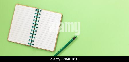 Blank open spiral notepad. Paper notebook and pencil with eraser on light green background. Space for text, overhead view Stock Photo