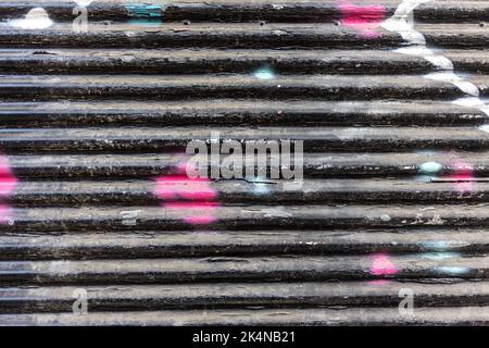 Old black with colorful spots empty roller shutter door background texture. Metal garage door construction, faded, old, closed, foldable. Copy space Stock Photo