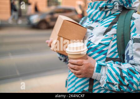 Craft packaging of delivered food in hands. Stack of food delivery boxes. Anonymous hands holding stack of delivery boxes and coffee cup.  Stock Photo