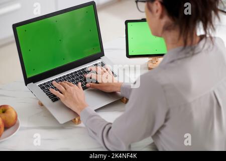 Close-up of young female programmer sitting in front of laptop with green screen and pressing buttons on keypad during work Stock Photo