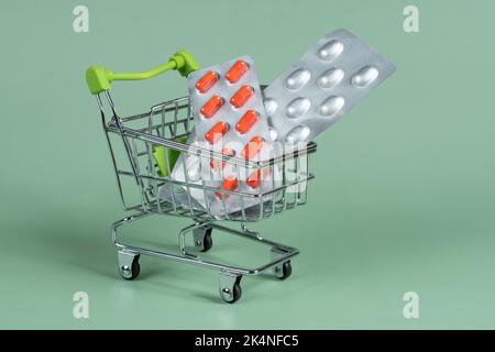 several different packages of pills in small shopping cart on green background, medicine order delivery concept Stock Photo