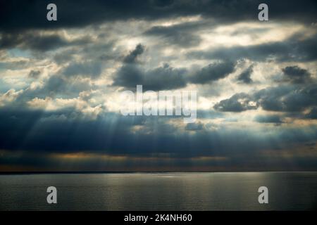 A dramatic sky over the sea with rays of light coming through the clouds Stock Photo