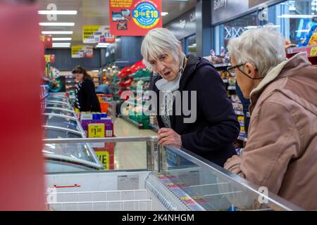 London, UK. Sept 29 2022 .Eldery woman shopper checking out the price of oven ready meal in refrigeration cabinet in Iceland store in Lewisham,London Stock Photo