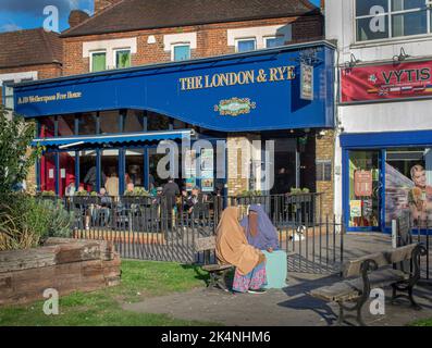 London, UK. Sept 29 2022 . Muslim woman sitting next to Weatherspoon Free House , The London & Rey pub . Stock Photo