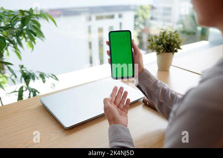 Hands of young female freelancer or software developer presenting new mobile application while holding smartphone with green screen Stock Photo