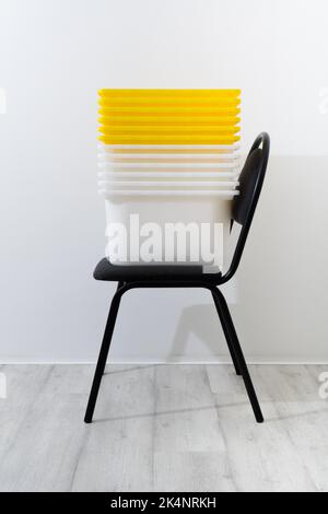 Yellow and white plastic containers on black office chair at home near white wall Stock Photo