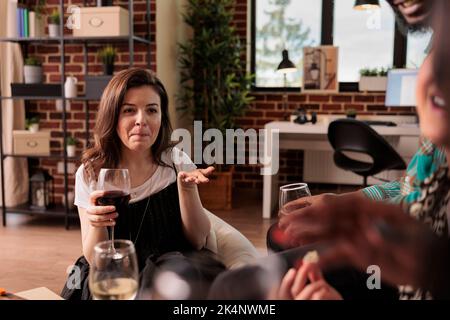 Unrecognizable different nationalities adult people group listening attentively young woman talk. Caucasian lady asking questions during friends gathering, drinking wine, eating snacks. Stock Photo