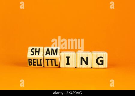 Shaming and belittling symbol. Concept words Shaming and Belittling on wooden cubes. Beautiful orange table orange background. Business shaming and be Stock Photo