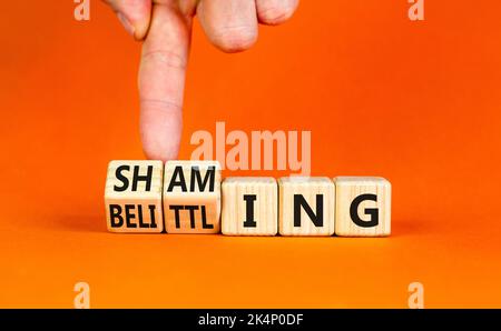 Shaming and belittling symbol. Concept words Shaming and Belittling on wooden cubes. Businessman hand. Beautiful orange table orange background. Busin Stock Photo