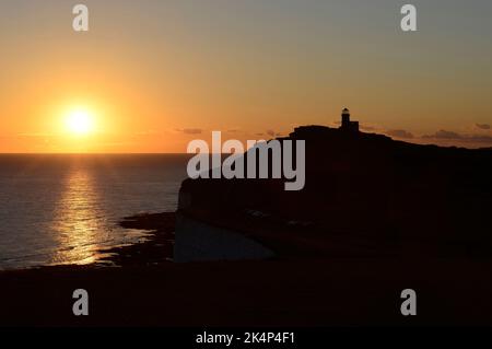 The sun sets over the sea behind the Belle Tout lighthouse between Beachy Head and Birling Gap on the sough coast near Eastbourne. Stock Photo