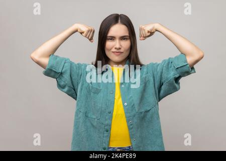 I am strong and independent. Confident proud woman showing biceps, expressing power ambitions to become successful, feminism concept, female rights. Indoor studio shot isolated on gray background. Stock Photo