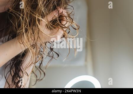 Woman scrunching her hair to form curls. Applying curly method for hair styling Stock Photo