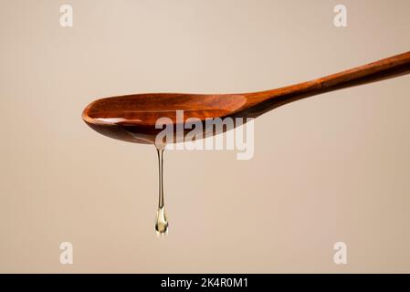 Honey and wooden spoon on beige background. Honey dripping from spoon. Close-up. Stock Photo