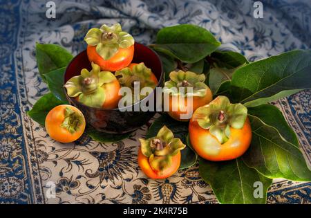 fresh ripe persimmons on patterned fabric cloth background Stock Photo