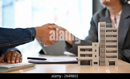 Modern urban building or condominium model on the table with a blurred background of two businesspeople shaking hands. real estate agent concept Stock Photo