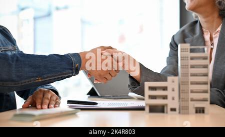 A professional senior Asian female realtor or real estate broker shaking hands with a male client after finished the meeting. cropped and close-up ima Stock Photo