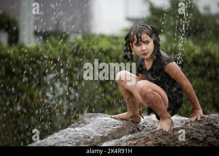 Cheerful child girl playing on heap of wet soil during raining in rainy season. Stock Photo