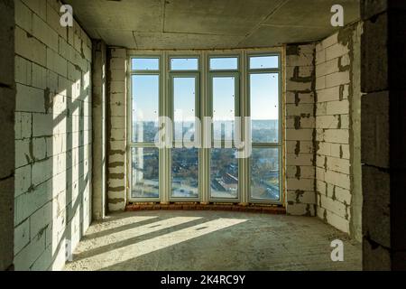 Empty draft rooms in a high-rise building under construction. Shadows from window frames on the wall on a sunny day Stock Photo