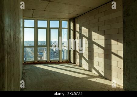 Empty draft rooms in a high-rise building under construction. Shadows from window frames on the wall on a sunny day Stock Photo