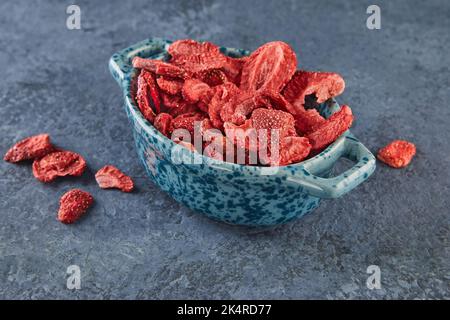 Strawberry chips stacked in ceramic dish on a gray-blue concrete background. Hundred-percent natural freeze-dried strawberries Stock Photo