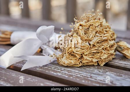 Bouquet of dried roses tied with white ribbon lying on bench at sunset Stock Photo