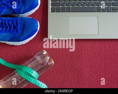 Sneakers, laptop, water bottle and measuring tape on a red yoga mat Stock Photo