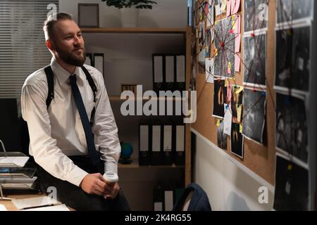 Detective looking at evidence board with photos in office, working at night Stock Photo