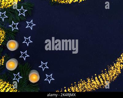 White shiny stars, burning candles, fir branches on black background with defocused lights. Christmas, New Year, holiday. Copy space Stock Photo