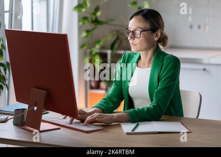 Successful focused Caucasian businesswoman working on computer typing e-mail sits at office desk Stock Photo