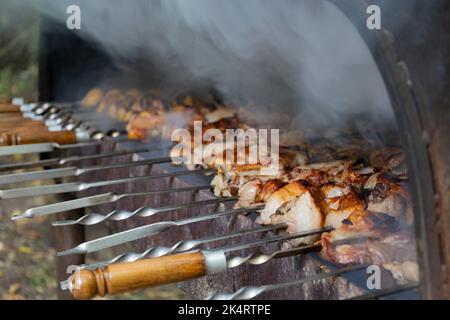 Close-up view of cooking delicious barbecue in a brazier. Tasty pork meat and potatoes are roasted on the grill. Smoke comes from preparing a barbecue Stock Photo