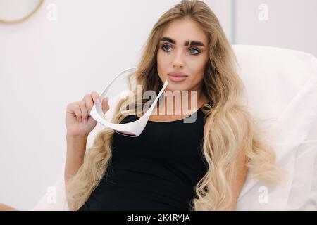 Beautiful model wears protective glasses before starting laser light hair removal. Treatment for hairless smooth skin at cosmetology salon Stock Photo