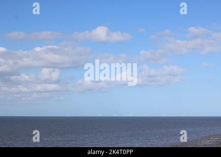 Wind farm on horizon at sea with dark blue sea below and pale blue sky above Stock Photo